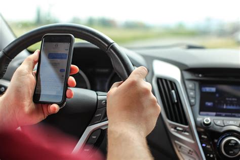 Vairuotojas naudojasi mobiliuoju telefonu prie vairo