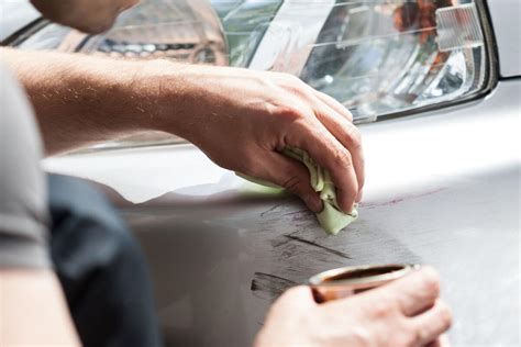 Rankos su dažų teptuku taisant automobilio įbrėžimą